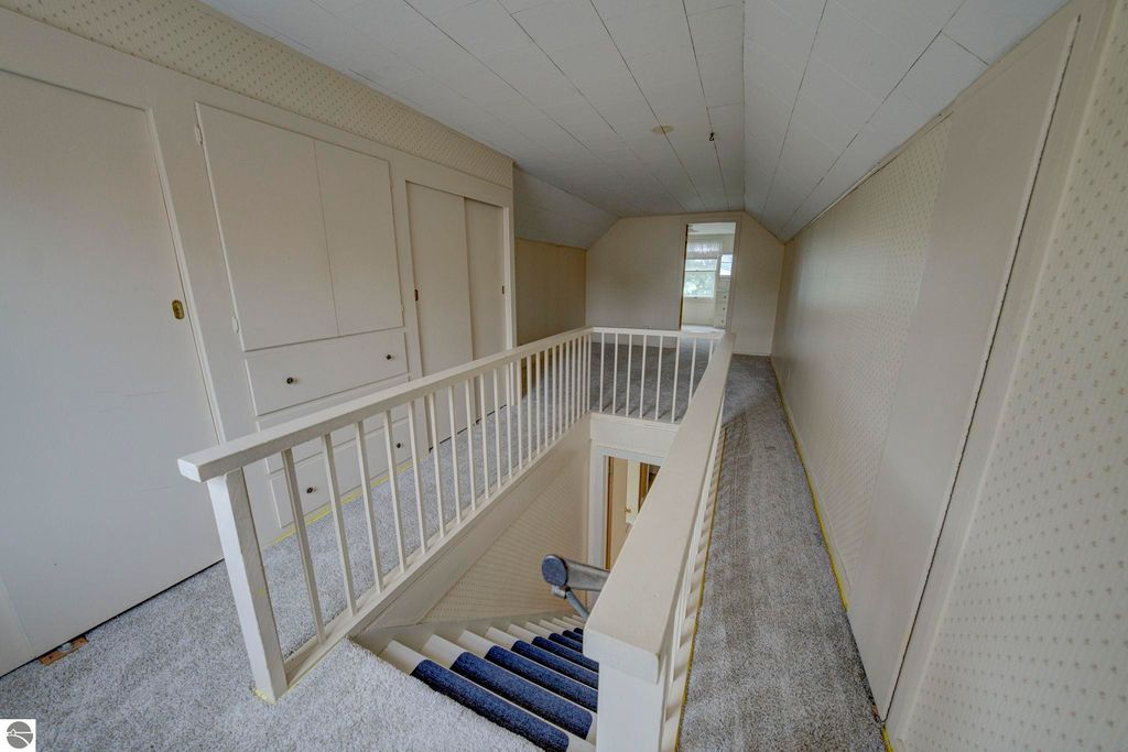 Upstairs hallway with white railings, plush carpeting, and built-in storage, leading to a den area and third bedroom in a well-maintained home at 624 Fenton Street, Kingsley, MI.