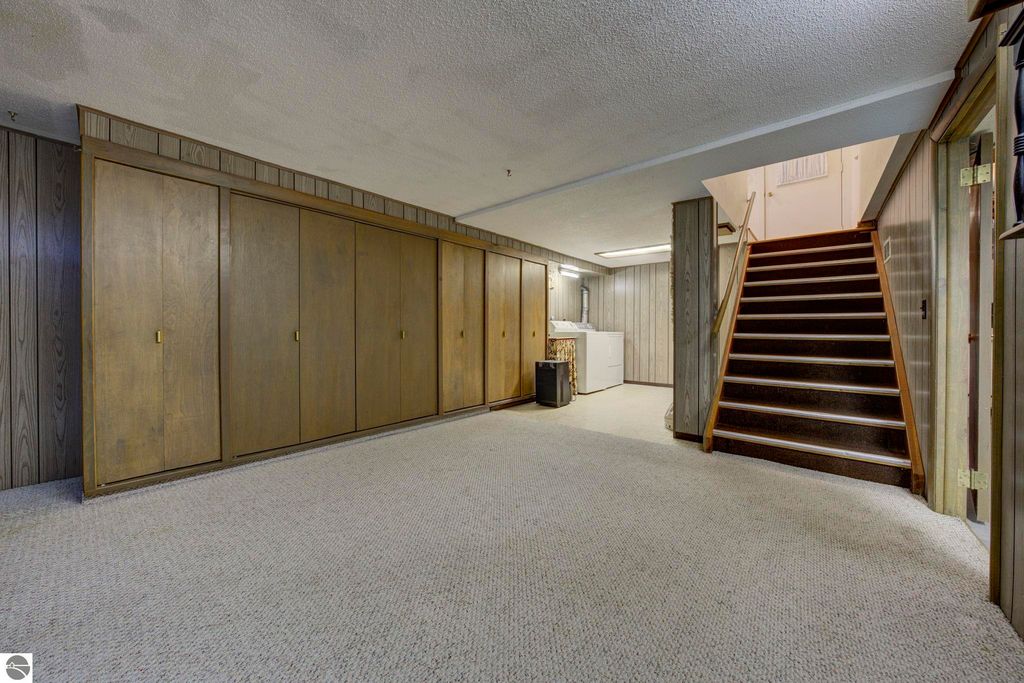Basement rec-room with built-in cabinets, laundry area, and staircase leading to upper floors in the home at 624 Fenton Street, Kingsley, MI.