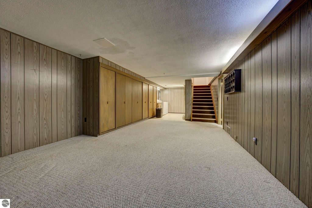 Basement rec-room with carpeted flooring, wooden paneling, built-in storage cabinets, and a staircase leading to the upper level.