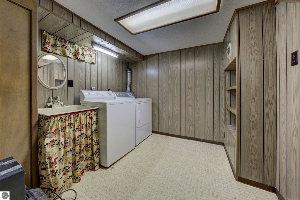 Laundry room with washing machine, sink, and built-in shelves, featuring wood paneling and decorative curtain, in a well-maintained home at 624 Fenton Street, Kingsley, MI.