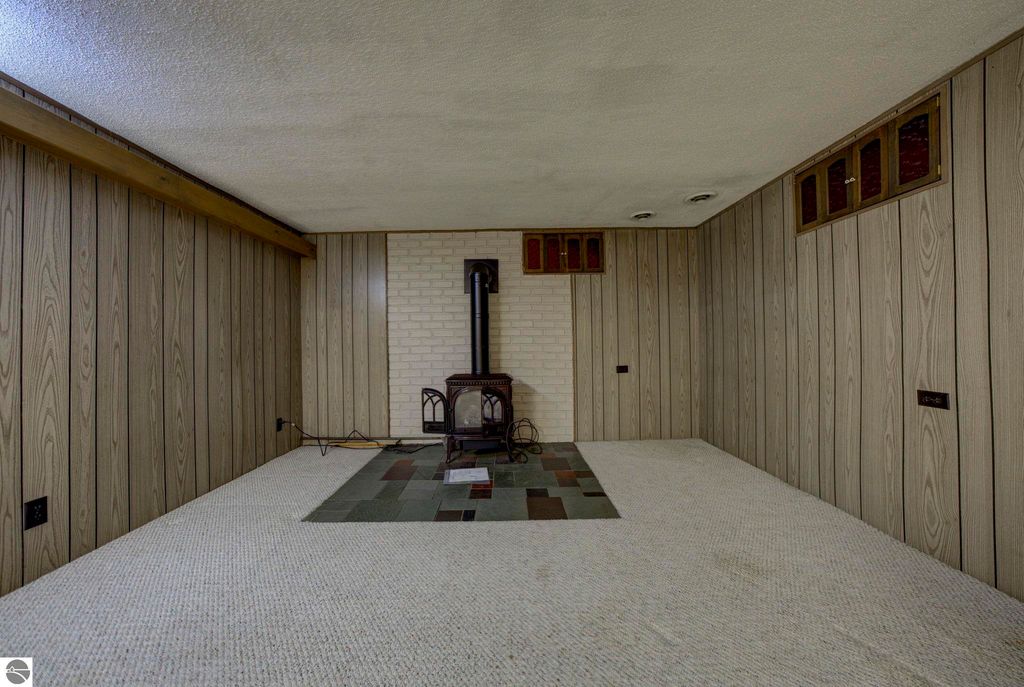 Basement rec-room featuring a brick fireplace, wood-paneled walls, and carpeted flooring, showcasing potential for a cozy living space in the home at 624 Fenton Street, Kingsley, MI.