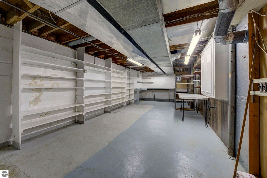 Basement storage area featuring white shelving units, a worktable, and exposed ductwork, highlighting ample organization space for crafts or workshop activities in the home at 624 Fenton Street, Kingsley, MI.
