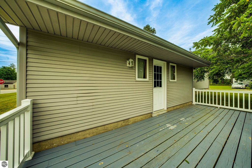 Side view of a well-maintained home at 624 Fenton Street, featuring a covered porch, light gray siding, and a wooden deck, with nearby greenery and a stop sign visible.
