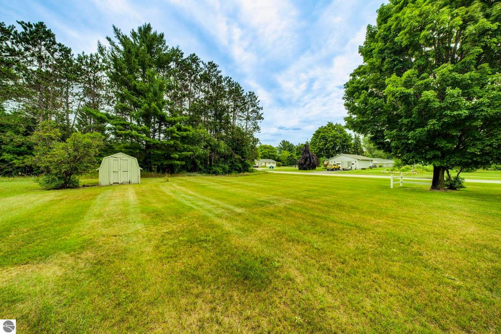 Expansive green lawn at 624 Fenton Street, featuring a storage shed, surrounded by trees and neighboring homes, ideal for potential buyers seeking a spacious property in Kingsley, MI.