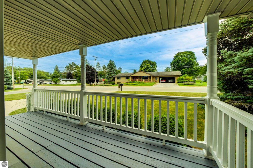 View from the covered front porch of a well-maintained home at 624 Fenton Street, Kingsley, MI, showcasing the surrounding neighborhood and grassy lawns.