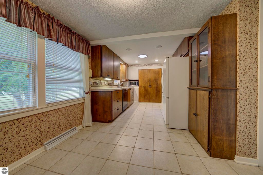 Bright and inviting galley kitchen with wooden cabinets, tiled flooring, and natural light from windows, showcasing a well-maintained home at 624 Fenton Street, Kingsley, MI.