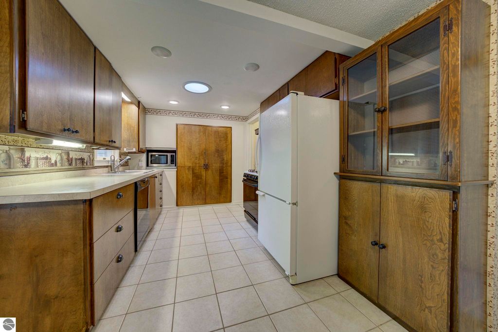 Kitchen interior featuring wooden cabinetry, white refrigerator, tile flooring, and natural light from a ceiling fixture, showcasing the open concept design of the home at 624 Fenton Street, Kingsley, MI.