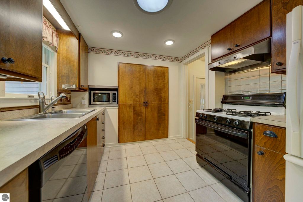 Kitchen interior featuring wooden cabinets, stainless steel sink, gas stove, and microwave, showcasing the galley layout of the home at 624 Fenton Street, Kingsley, MI.