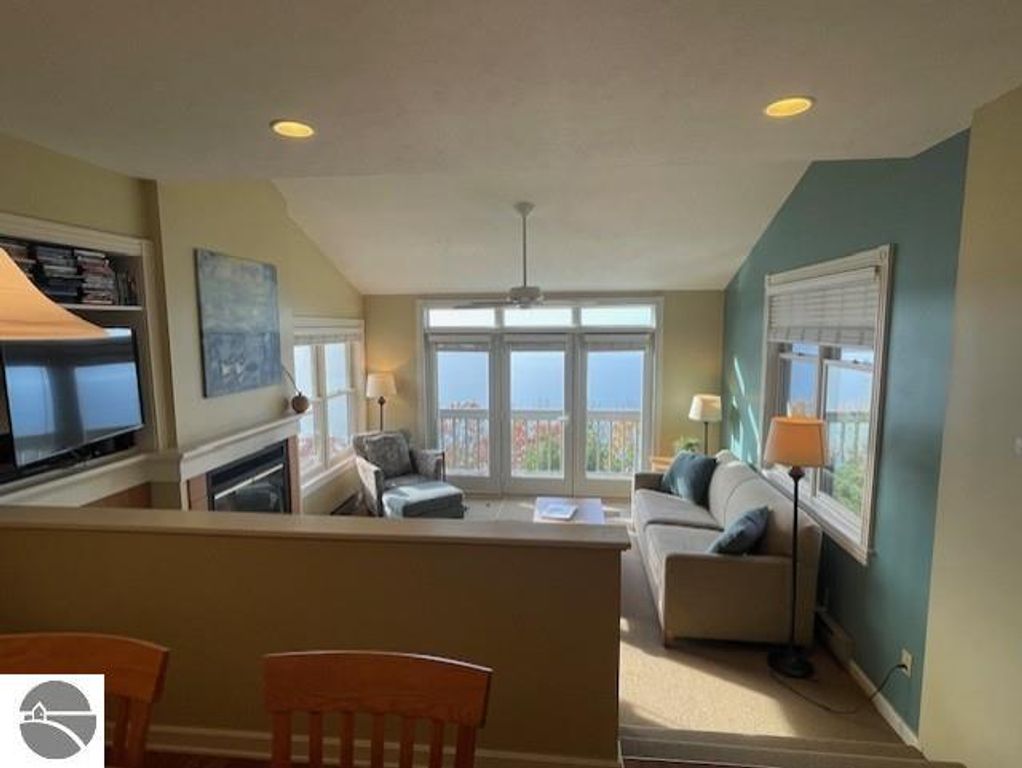 Living room interior of 12C Pinnacle Place, Glen Arbor, featuring panoramic Lake Michigan views, modern furnishings, fireplace, and two large windows.