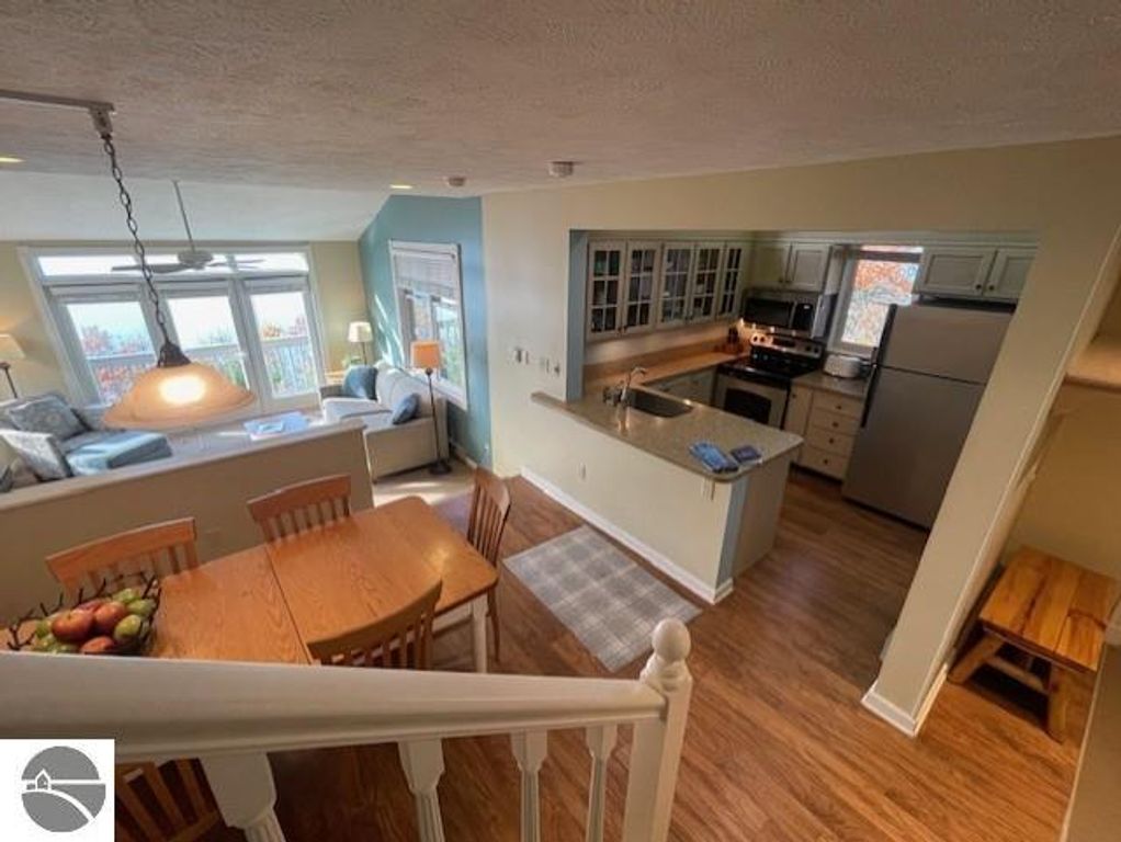 Interior view of 12C Pinnacle Place featuring a dining area with wooden table and chairs, modern kitchen with stainless steel appliances, and a cozy living space with large windows showcasing panoramic views of Lake Michigan.