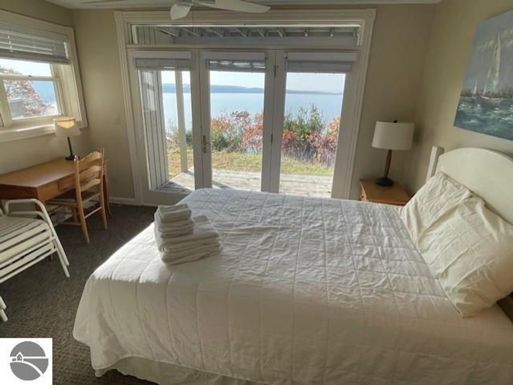 Bedroom interior of Pinnacle Place 12C with white bedding, desk, and large windows showcasing panoramic views of Lake Michigan and surrounding nature.