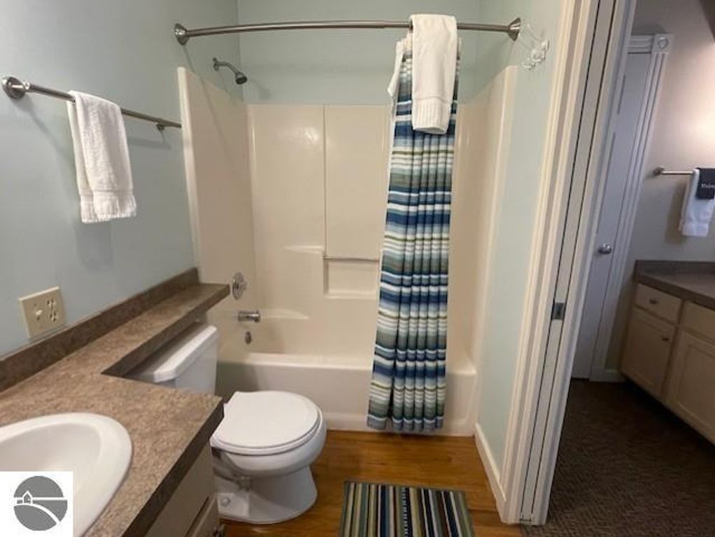 Bathroom interior featuring a bathtub with shower, striped shower curtain, toilet, and sink, showcasing updated furnishings in the Glen Arbor, MI property listing at 12C Pinnacle Place.