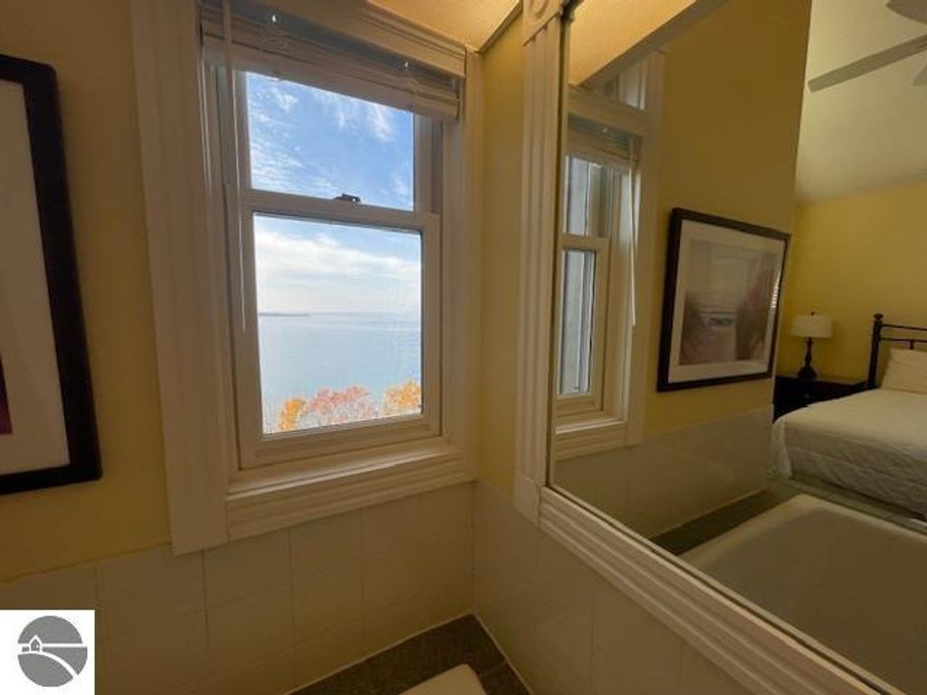 Interior view from a window in 12C Pinnacle Place, showcasing panoramic views of Lake Michigan, with a reflection in the mirror, bright yellow walls, and bedroom furnishings.