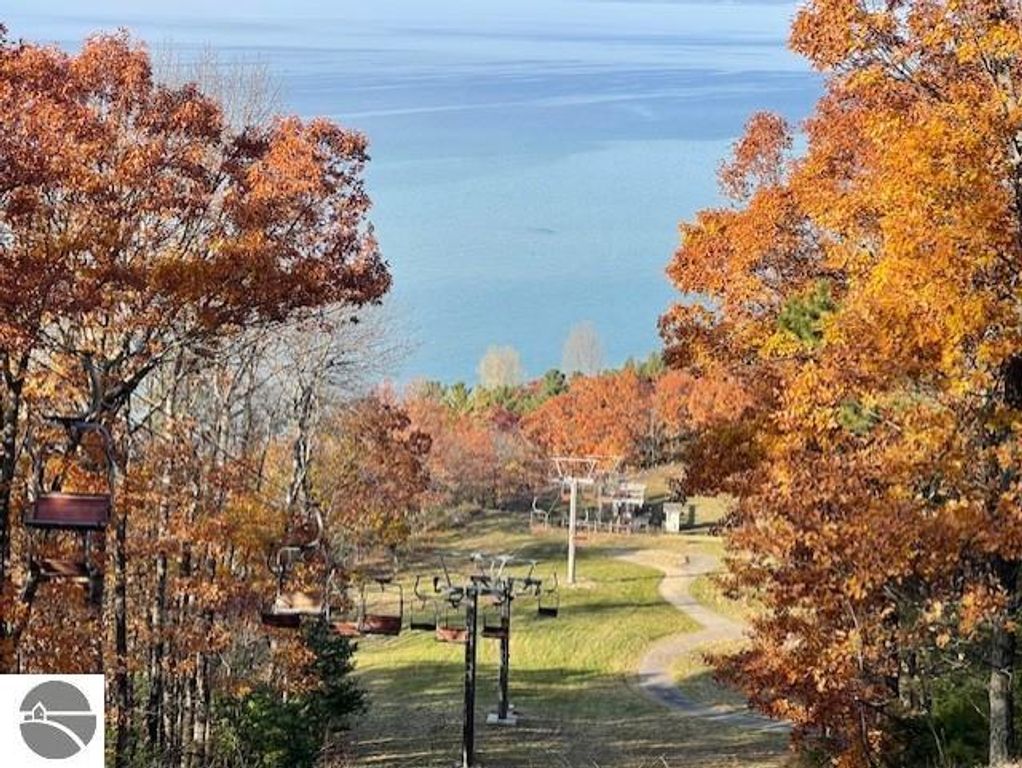 Autumn landscape view from Pinnacle Place, showcasing colorful foliage, ski lifts, and Lake Michigan in the background, highlighting the scenic location of the Glen Arbor property listing.