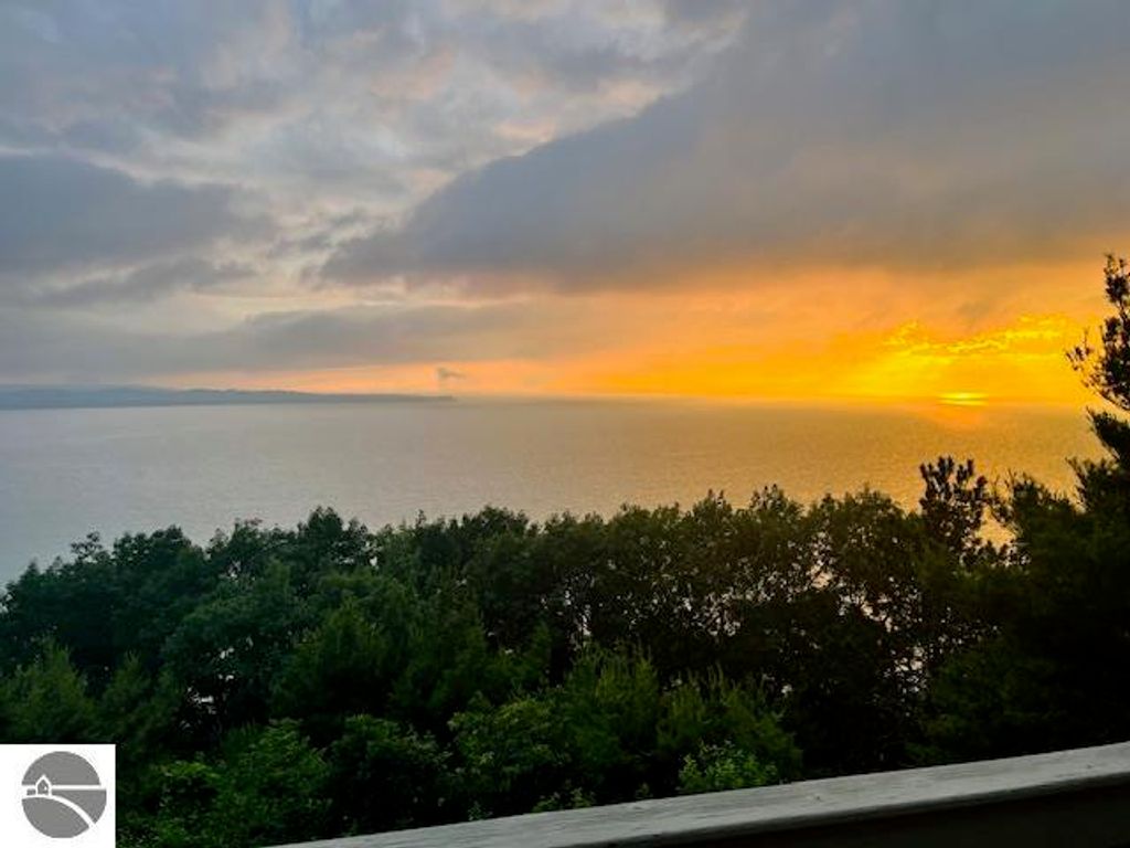 Panoramic view of Lake Michigan at sunset from Pinnacle Place, showcasing vibrant orange and yellow hues in the sky, framed by lush greenery.