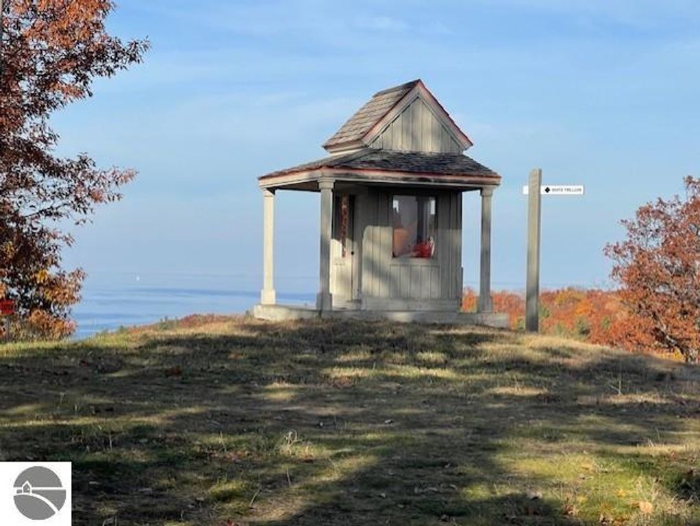 Scenic view of a gazebo on a hillside overlooking Lake Michigan, surrounded by autumn foliage, with a directional sign indicating nearby trails.