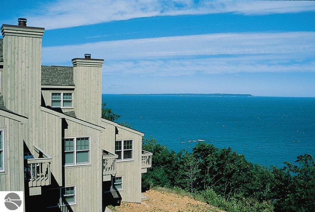 Exterior view of Pinnacle Place 12C in Glen Arbor, MI, showcasing the wooden structure, balconies, and panoramic Lake Michigan views with distant islands and blue skies.