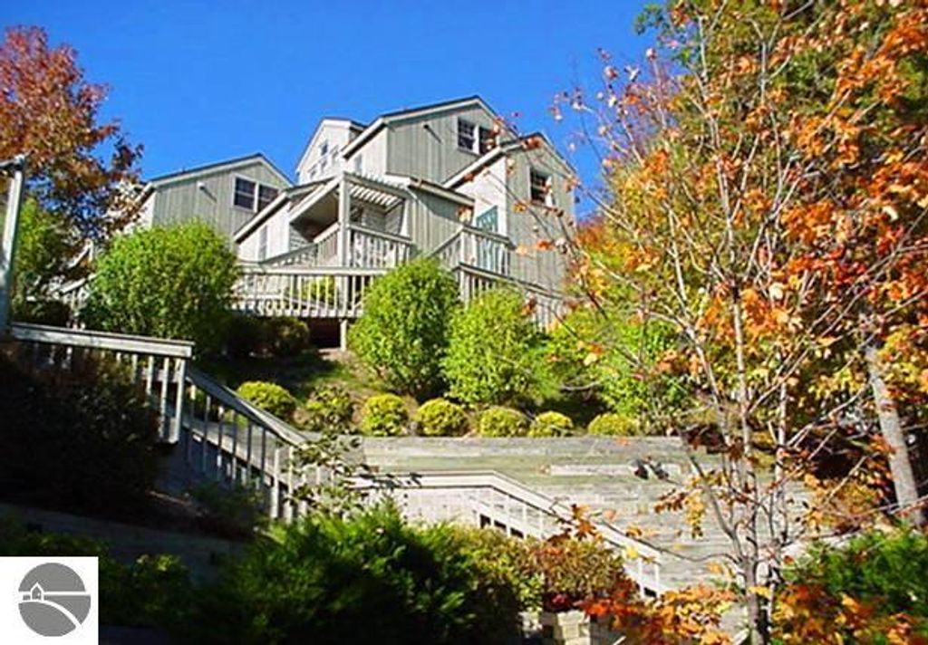 Exterior view of 12C Pinnacle Place, Glen Arbor, MI, showcasing multi-level architecture, lush landscaping, and steps leading to the entrance, highlighting its appealing features and scenic surroundings.