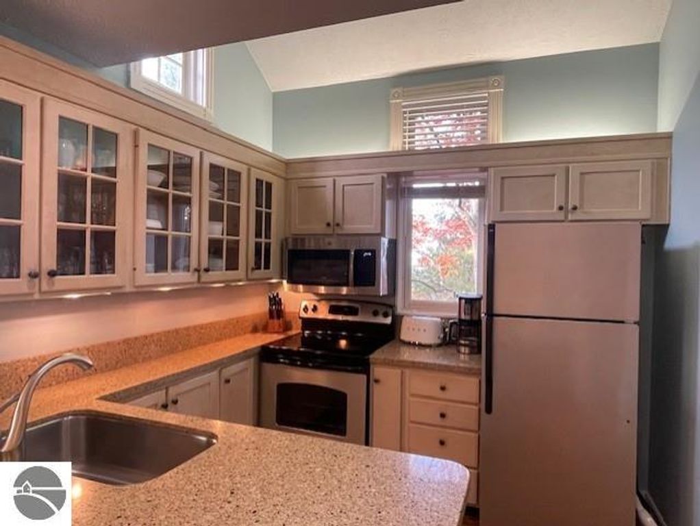 Modern kitchen interior with granite countertops, stainless steel appliances, and glass-front cabinets, featuring a window with a view, part of the Glen Arbor property listing at 12C Pinnacle Place.
