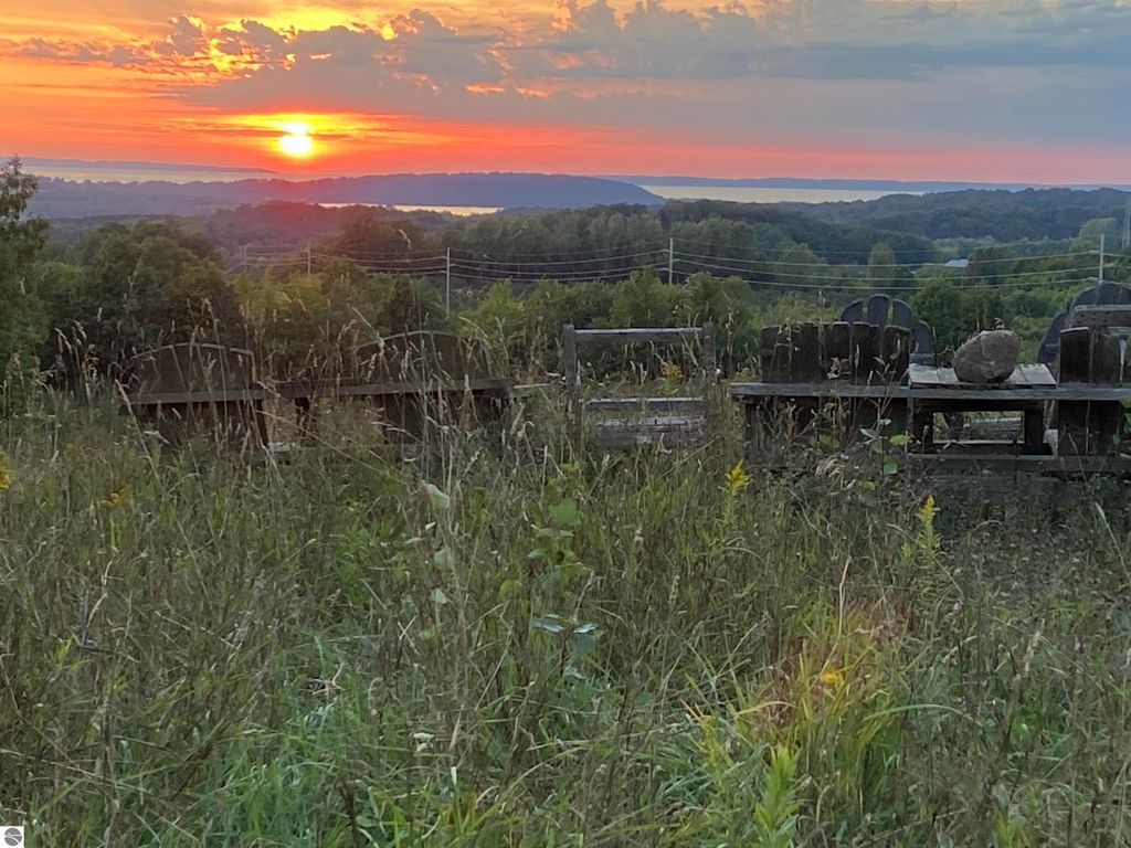 Sunset view over Lake Michigan from a ridge-top property in Suttons Bay, featuring silhouettes of wooden seating and lush greenery in the foreground, highlighting the scenic beauty and development potential of the land.