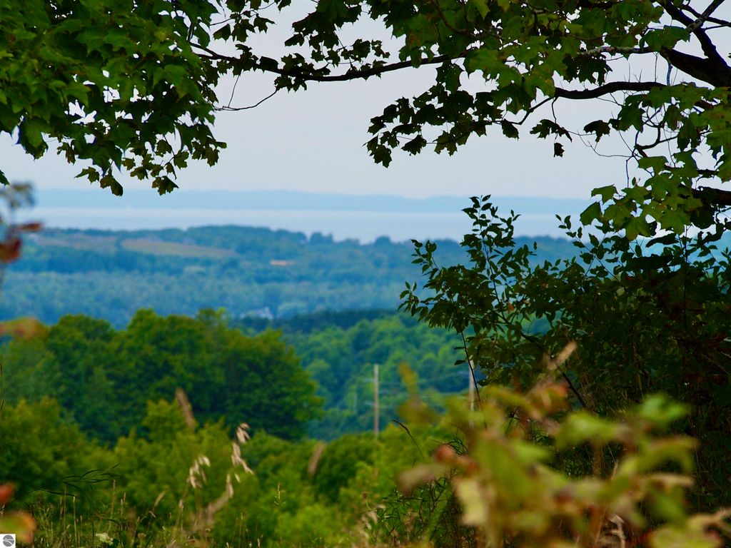 Scenic view from a high elevation overlooking lush green landscapes and distant water views, highlighting the development potential of the 72-acre parcel in Suttons Bay, MI.