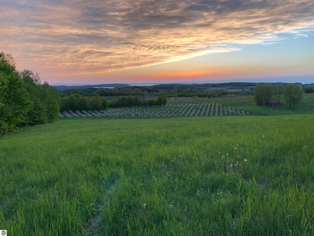 Breathtaking sunset view over expansive green fields and orchards in Suttons Bay, showcasing high-elevation farmland with sweeping landscapes and distant water views.