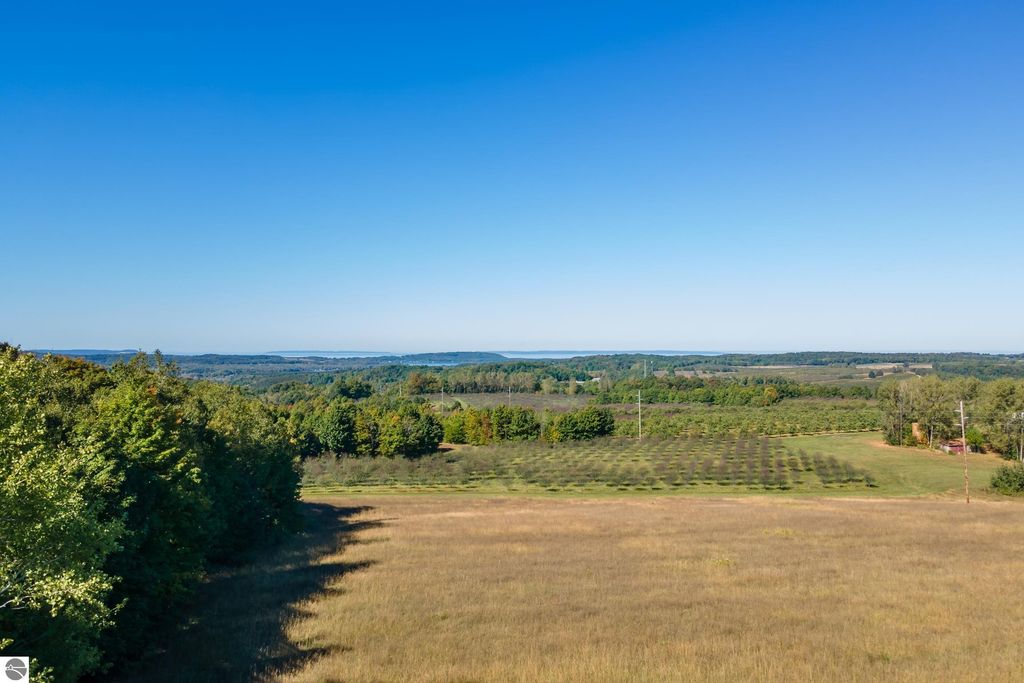 Expansive view of high-elevation farmland in Suttons Bay, MI, showcasing lush greenery, rolling hills, and distant water views, highlighting the scenic beauty and potential of the 74.2-acre development parcel.