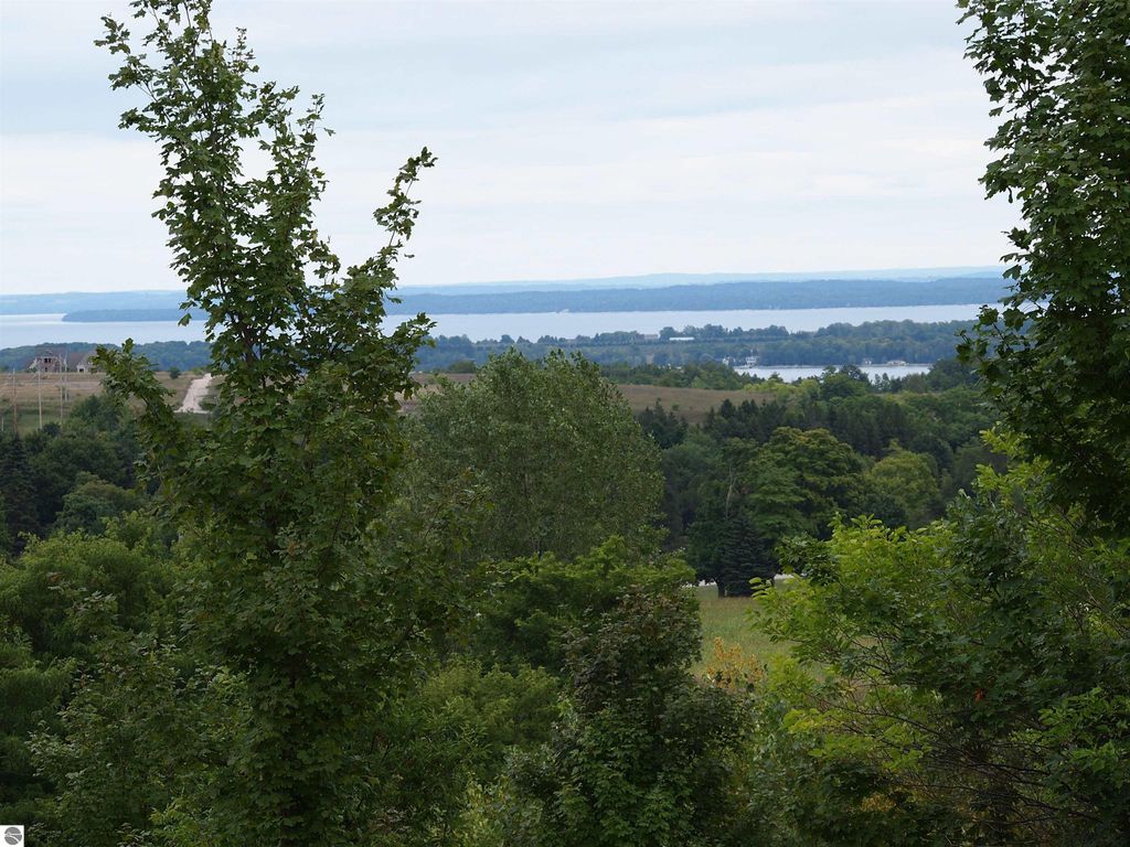 Breathtaking view from high-elevation farmland in Suttons Bay, showcasing lush greenery and expansive water vistas of Grand Traverse Bay and surrounding landscapes.