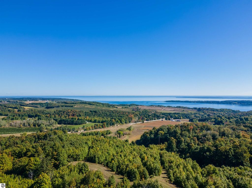 Aerial view of 72-acre ridge-top farmland in Suttons Bay, MI, showcasing sweeping water views of Grand Traverse Bay and Lake Michigan, surrounded by vibrant autumn foliage and rolling hills, highlighting the property's unique development potential.