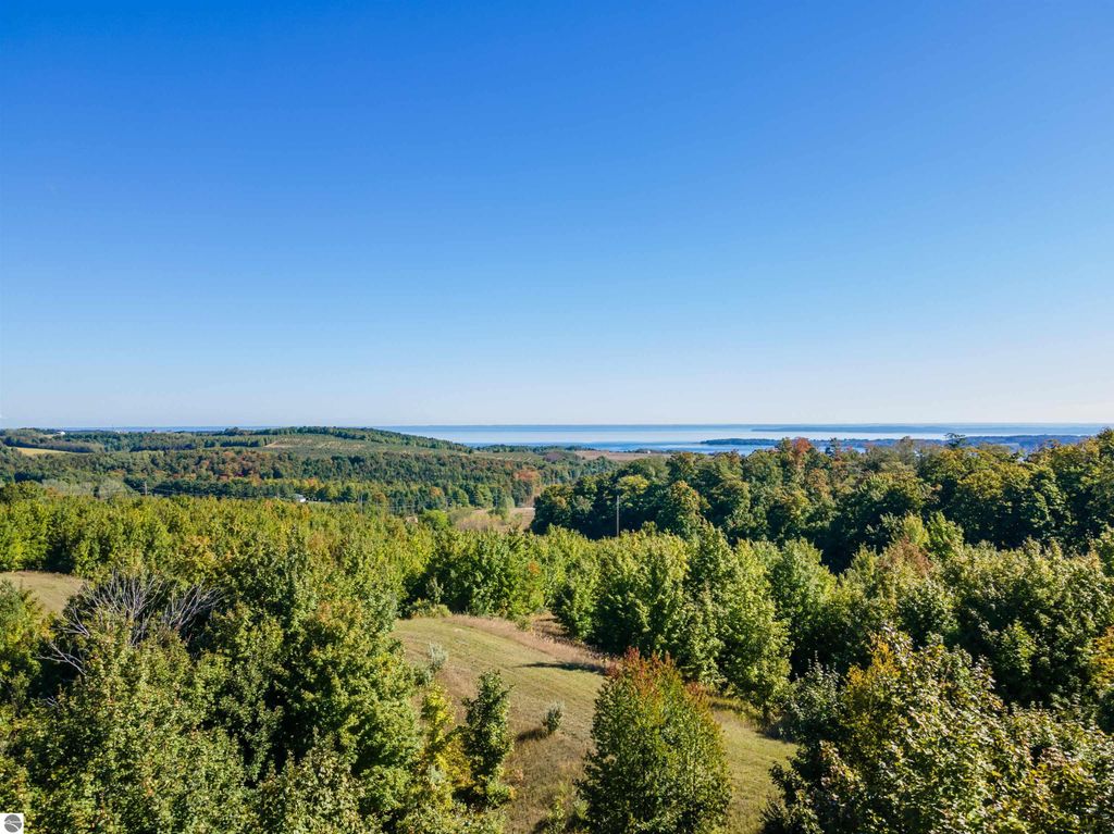 Breathtaking panoramic view from high-elevation farmland in Suttons Bay, showcasing vibrant autumn foliage, expansive landscapes, and distant water views of Grand Traverse Bay and Lake Michigan.