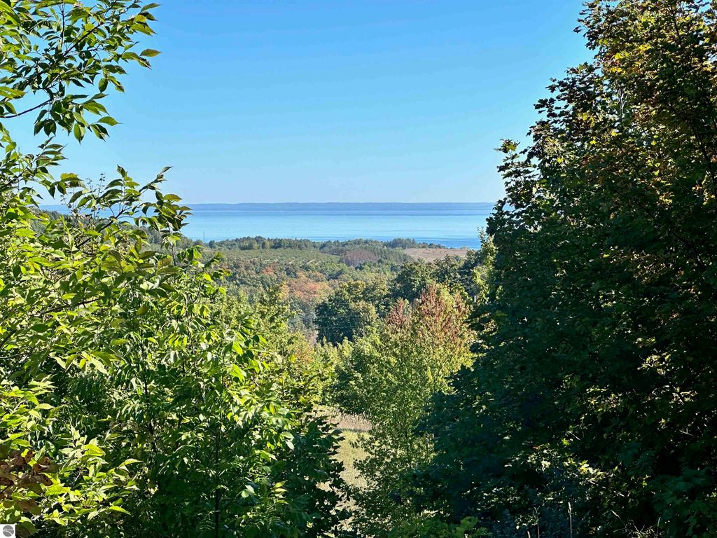 Scenic view of lush greenery framing expansive water vistas over Grand Traverse Bay and Suttons Bay, highlighting the stunning landscape of the 74.2-acre parcel in Suttons Bay, MI.