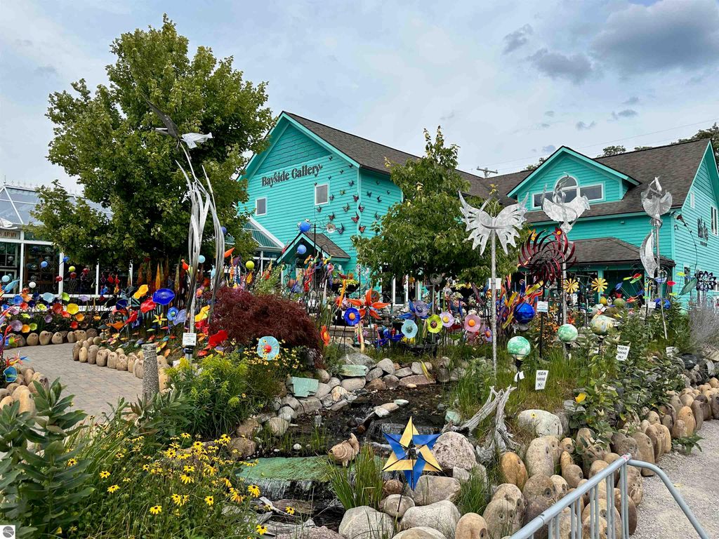 Bayside Gallery in Suttons Bay, MI, featuring vibrant outdoor art installations, colorful sculptures, and lush landscaping surrounding the turquoise building.