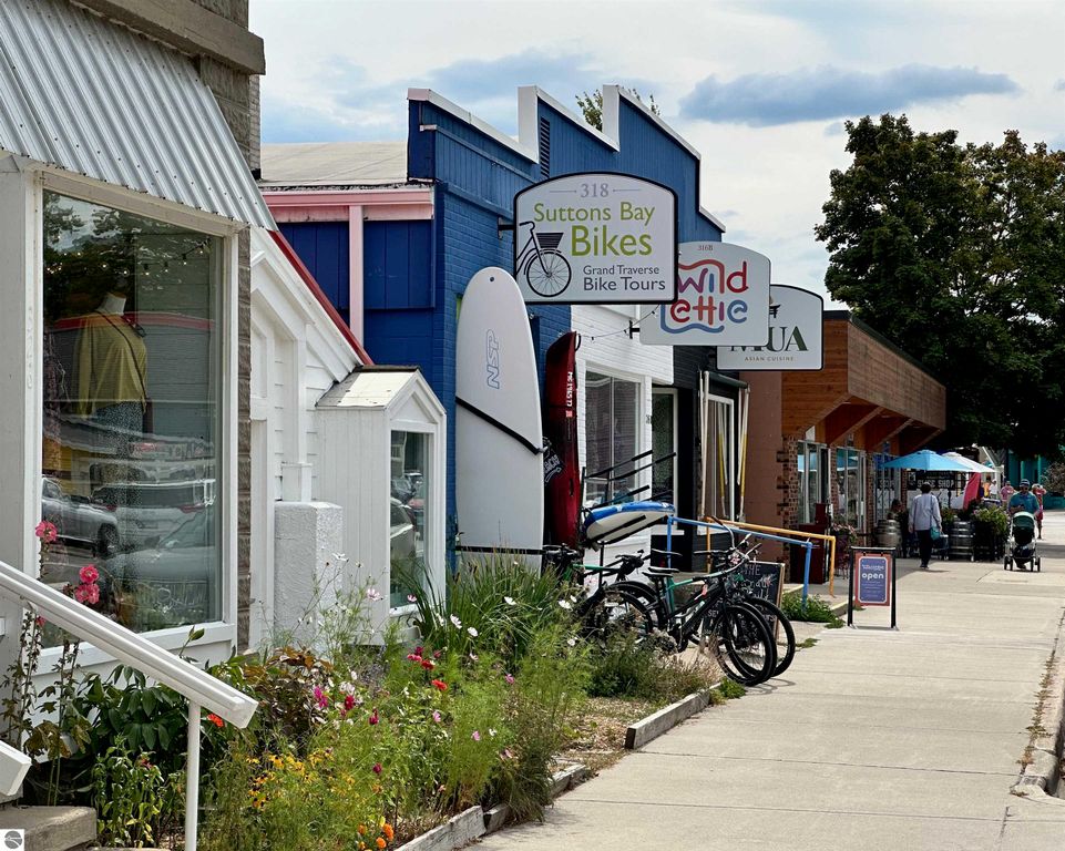 Suttons Bay storefronts featuring bike rental shop, colorful signage, and pedestrians enjoying the vibrant streetscape.