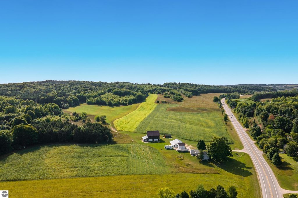 Aerial view of 74.2-acre parcel on E Duck Lake Road in Suttons Bay, MI, showcasing lush farmland, wooded areas, and scenic landscape with clear blue sky, ideal for luxury estate development or recreational use.
