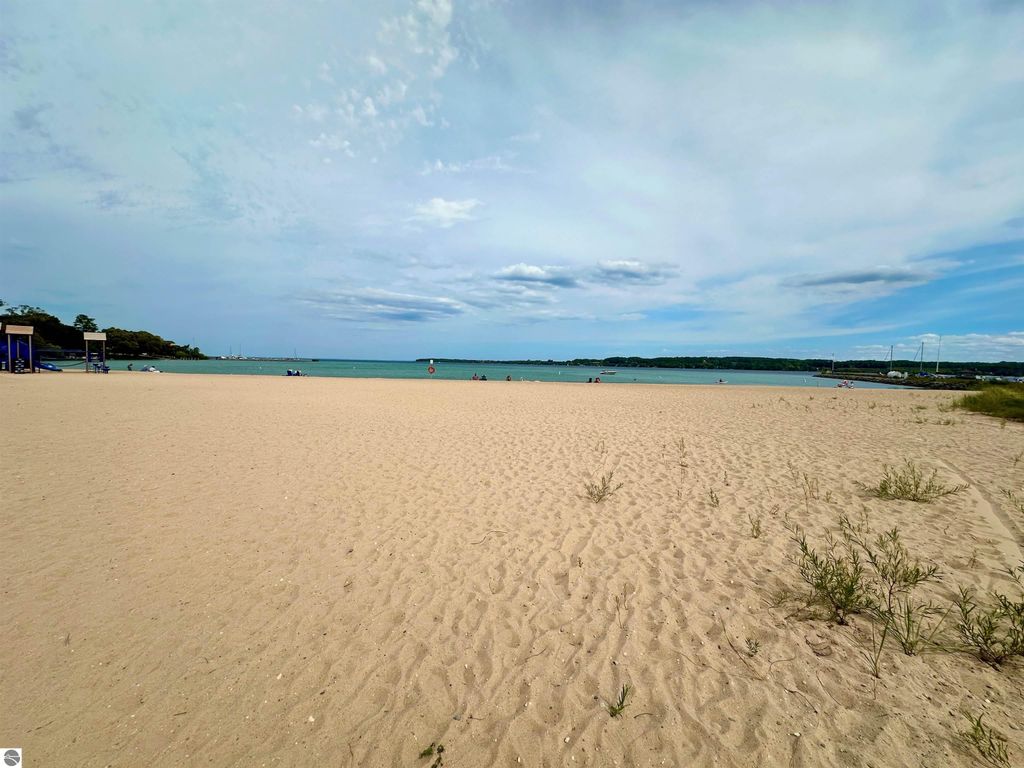 Sandy beach with clear blue water and distant shoreline, showcasing recreational area near Suttons Bay, MI, highlighting scenic views of Grand Traverse Bay.