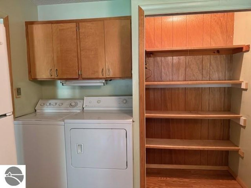 Laundry area featuring stacked washer and dryer with wooden cabinetry above and adjacent open shelving, part of the cottage at 6025 Forest Haven Drive, Glen Arbor, MI.