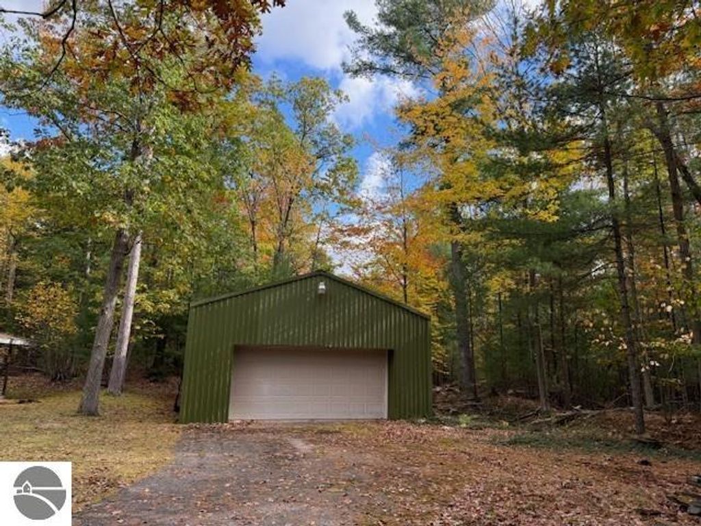 Green pole building surrounded by autumn foliage on wooded lot at 6025 Forest Haven Drive, Glen Arbor, MI, showcasing potential for storage or guest suite.