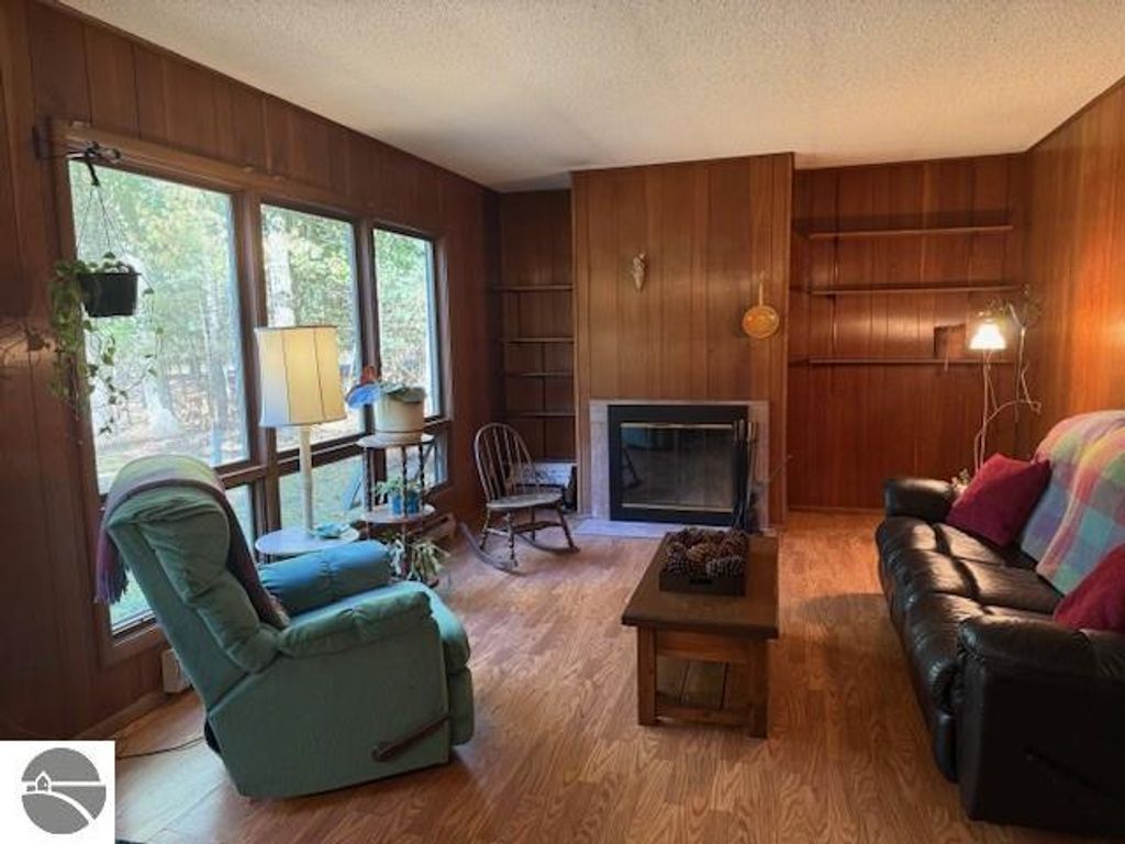 Cozy living room in Glen Arbor cottage featuring a green recliner, black leather sofa, wooden coffee table, and large windows overlooking wooded scenery.