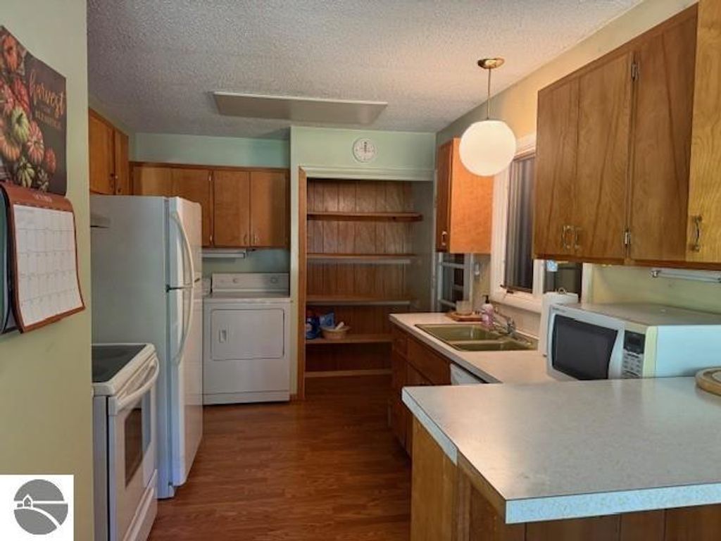 Kitchen interior featuring wooden cabinets, white appliances, and a light fixture, showcasing a cozy, functional space in a cottage for sale in Glen Arbor, MI.