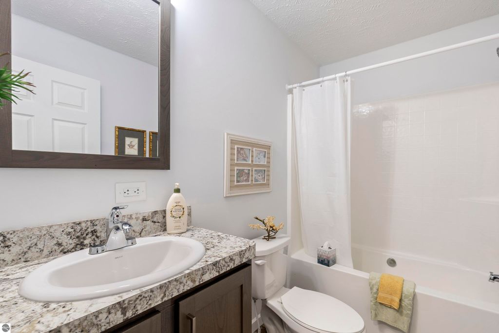 Bathroom with modern fixtures, granite countertop, sink, mirror, and shower curtain, showcasing a clean and inviting space in a new home for sale in Interlochen, MI.
