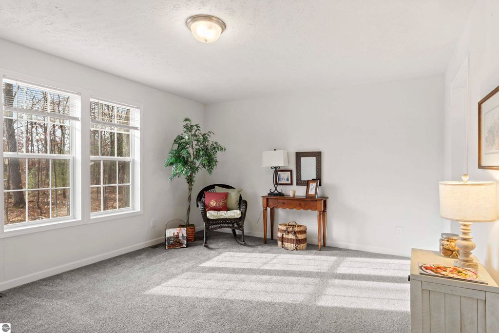 Bright, inviting living room in new ranch home at 11754 Country Acres Drive, featuring large windows, plush carpet, decorative lamp, and a small table with framed pictures, surrounded by natural scenery.