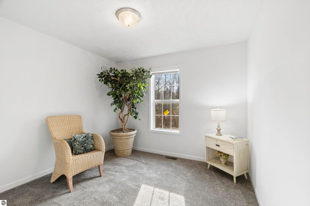 Cozy interior of a newly built home featuring a wicker armchair, indoor plant, and a small side table with a lamp, showcasing bright natural light from a window in Interlochen, MI.