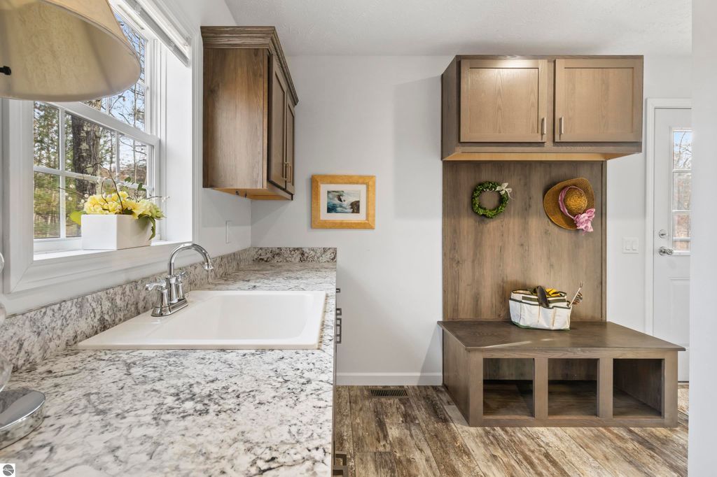 Modern kitchen interior featuring granite countertops, a stainless steel sink, and wooden cabinetry, with a cozy mudroom area showcasing decorative items and storage space.
