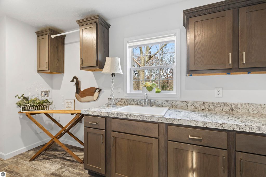 Modern kitchen with granite countertop, wooden cabinets, and window overlooking trees, featuring a sink and a decorative duck figurine.