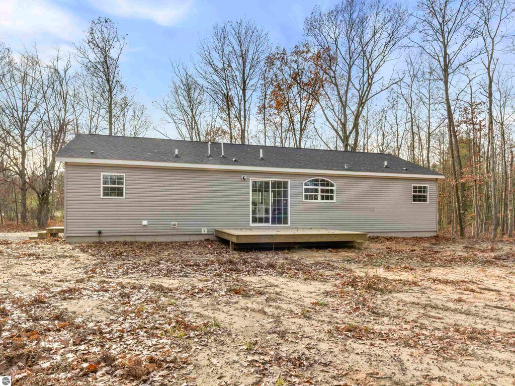 New ranch-style home with a wooden deck, situated on a 2.5-acre corner lot in Interlochen, MI, surrounded by trees and autumn foliage.