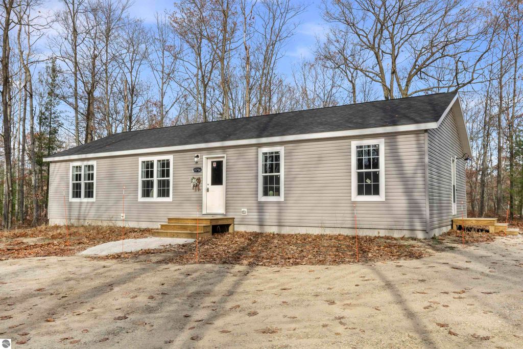Newly constructed ranch-style home at 11754 Country Acres Drive, Interlochen, MI, featuring three bedrooms, two bathrooms, surrounded by trees on a 2.5-acre corner lot.