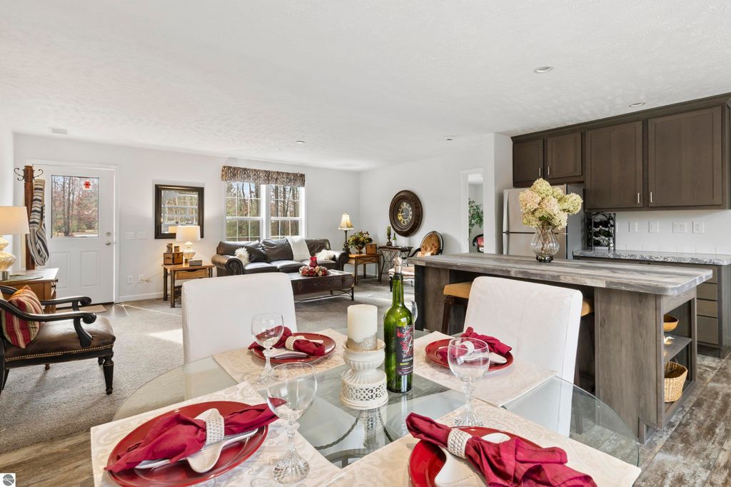 Modern open-concept living space in a new ranch home, featuring a dining area with elegant table settings, a cozy living area with natural light, and a kitchen with dark cabinetry, located at 11754 Country Acres Drive, Interlochen, MI.