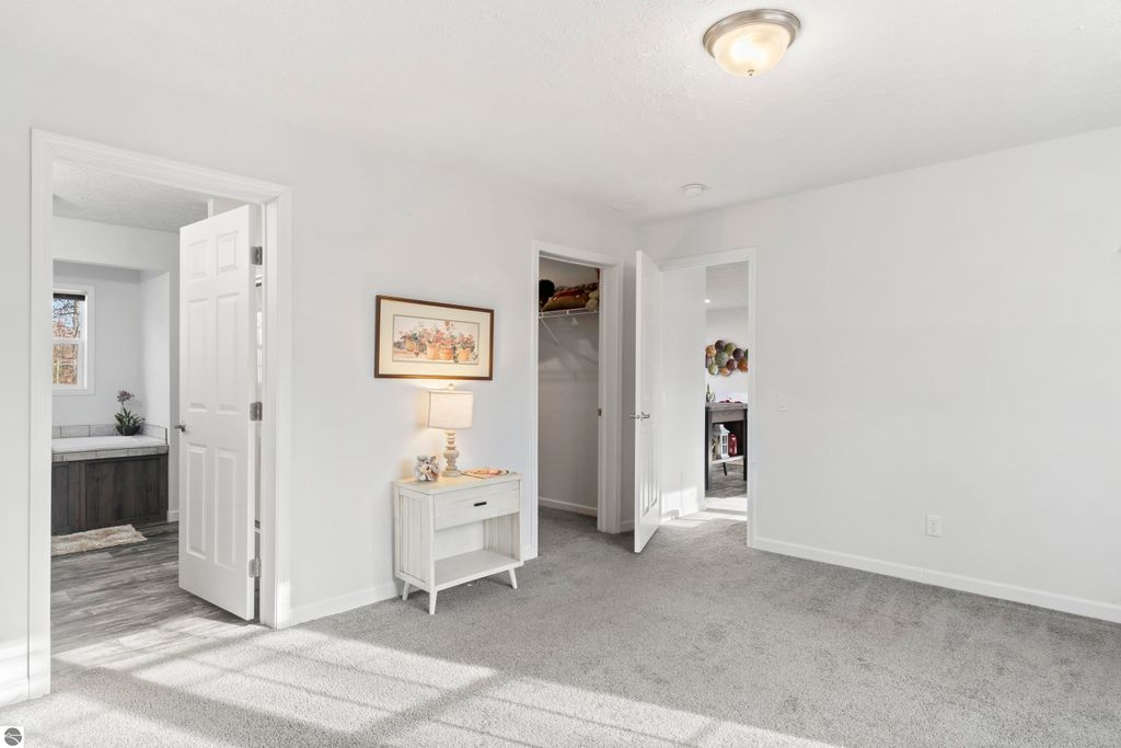 Bright interior of a new home featuring a cozy living space with a decorative lamp and framed artwork, open doors leading to a bathroom and closet, and plush carpeting, showcasing the comfort and modern design of the 3-bedroom ranch at 11754 Country Acres Drive, Interlochen, MI.
