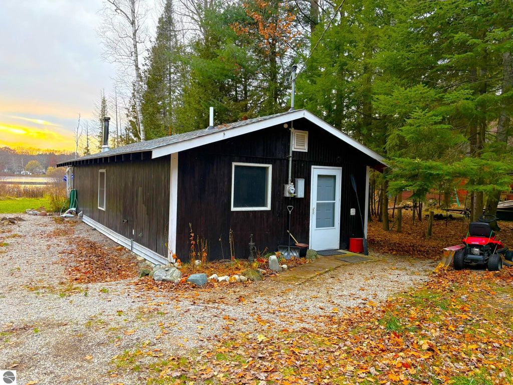 Waterfront cottage at 2456 Birch Road, Grawn, MI, featuring a dark exterior, surrounded by trees and autumn foliage, with a gravel driveway and nearby lake view.
