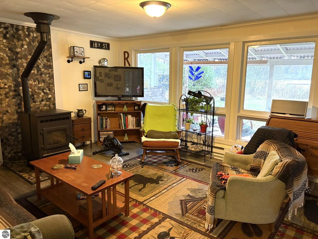 Cozy living room featuring a pellet stove, comfortable seating, decorative rug, and large windows overlooking nature, ideal for a waterfront cottage lifestyle in Grawn, MI.